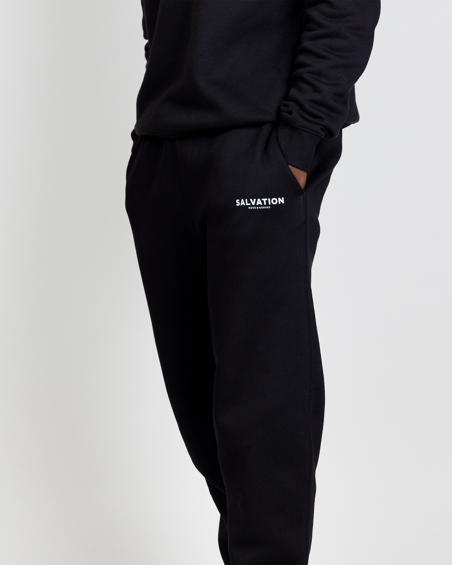 Faith-inspired track pants in black featuring Salvation text logo, jersey lined pockets, and clean streetwear style.
